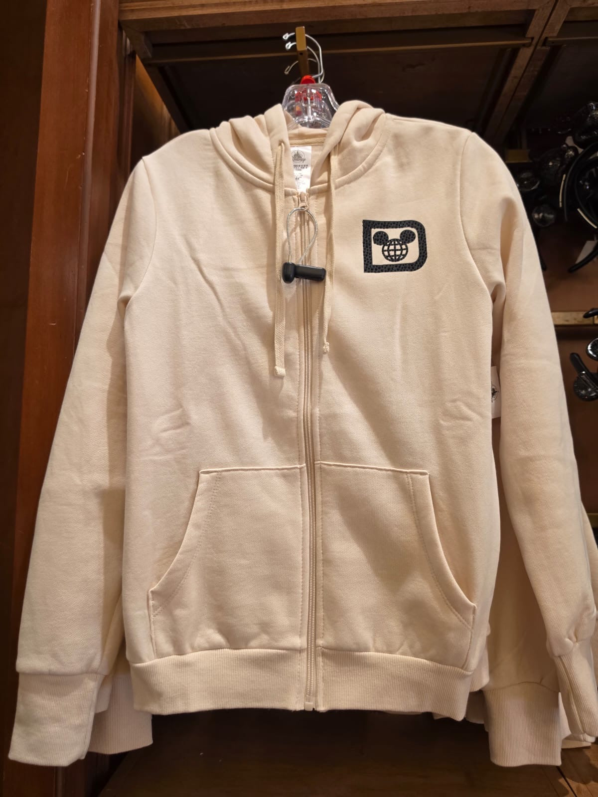 Beige hoodie with a logo on a hanger against a wooden background