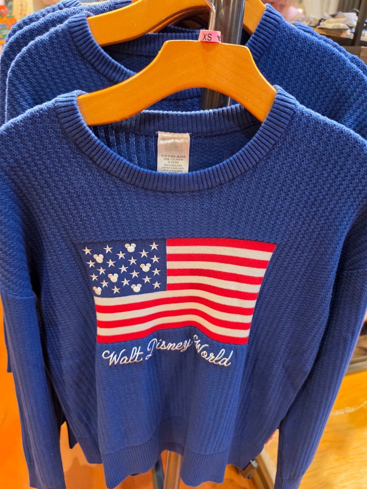 Blue sweater with American flag design and 'Walt Disney World' text on a hanger.