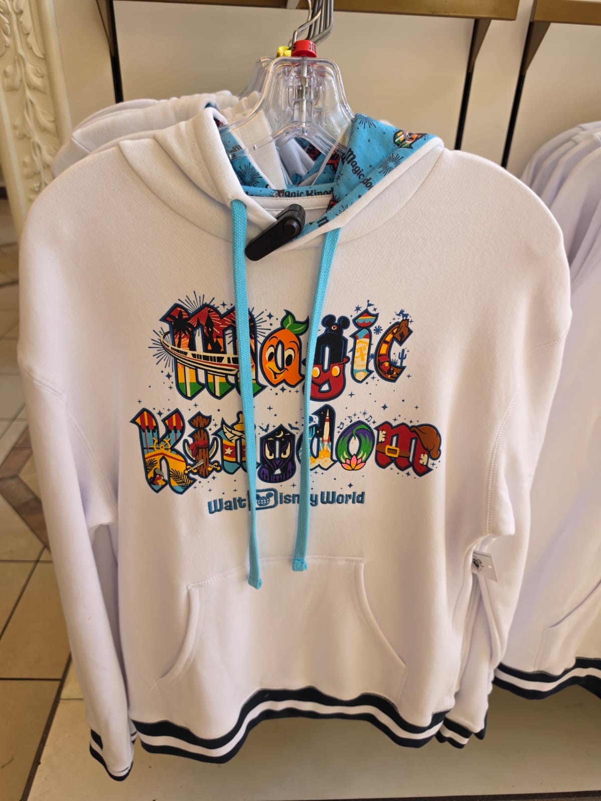 White hoodie with colorful 'Magic Kingdom' text on a hanger.
