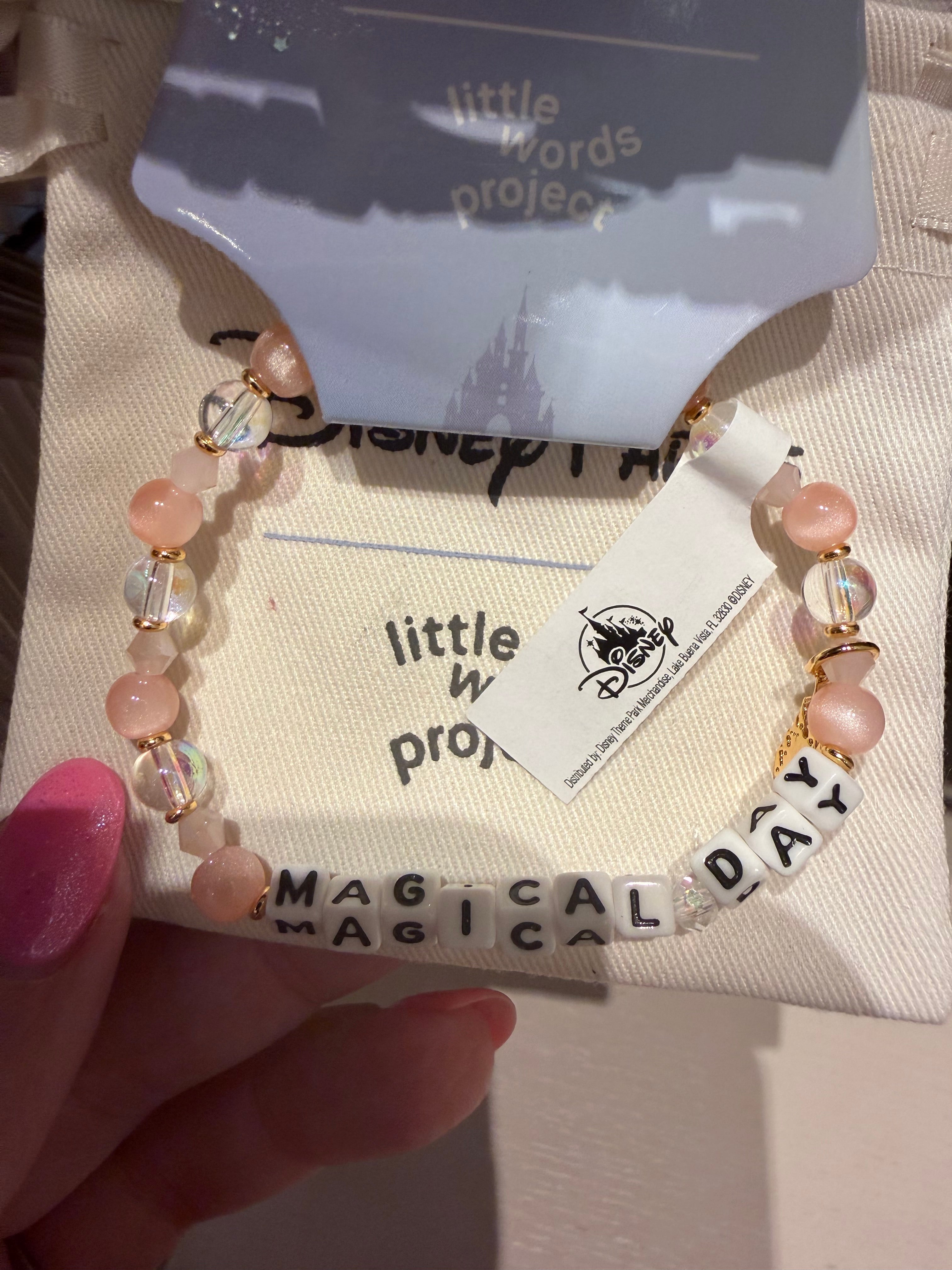 Bracelet with 'MAGICAL DAY' beads held over a 'little words project' card.